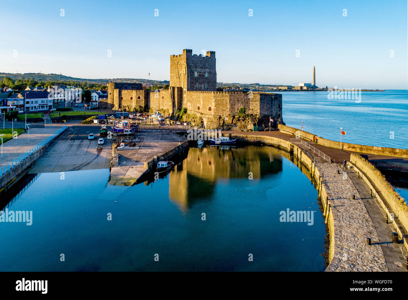Medieval Norman Castle and harbor with boat ramp and wave breaker in Carrickfergus near Belfast, Northern Ireland, UK. Aerial view in sunset light. Stock Photo