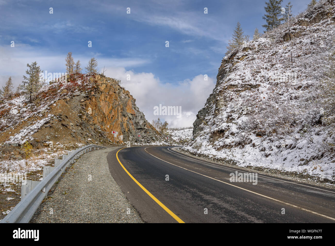 Scenic view of the hairpin bend wet winding road through the pass, part of the mountain serpentine, in autumn cloudy weather with first snow Stock Photo