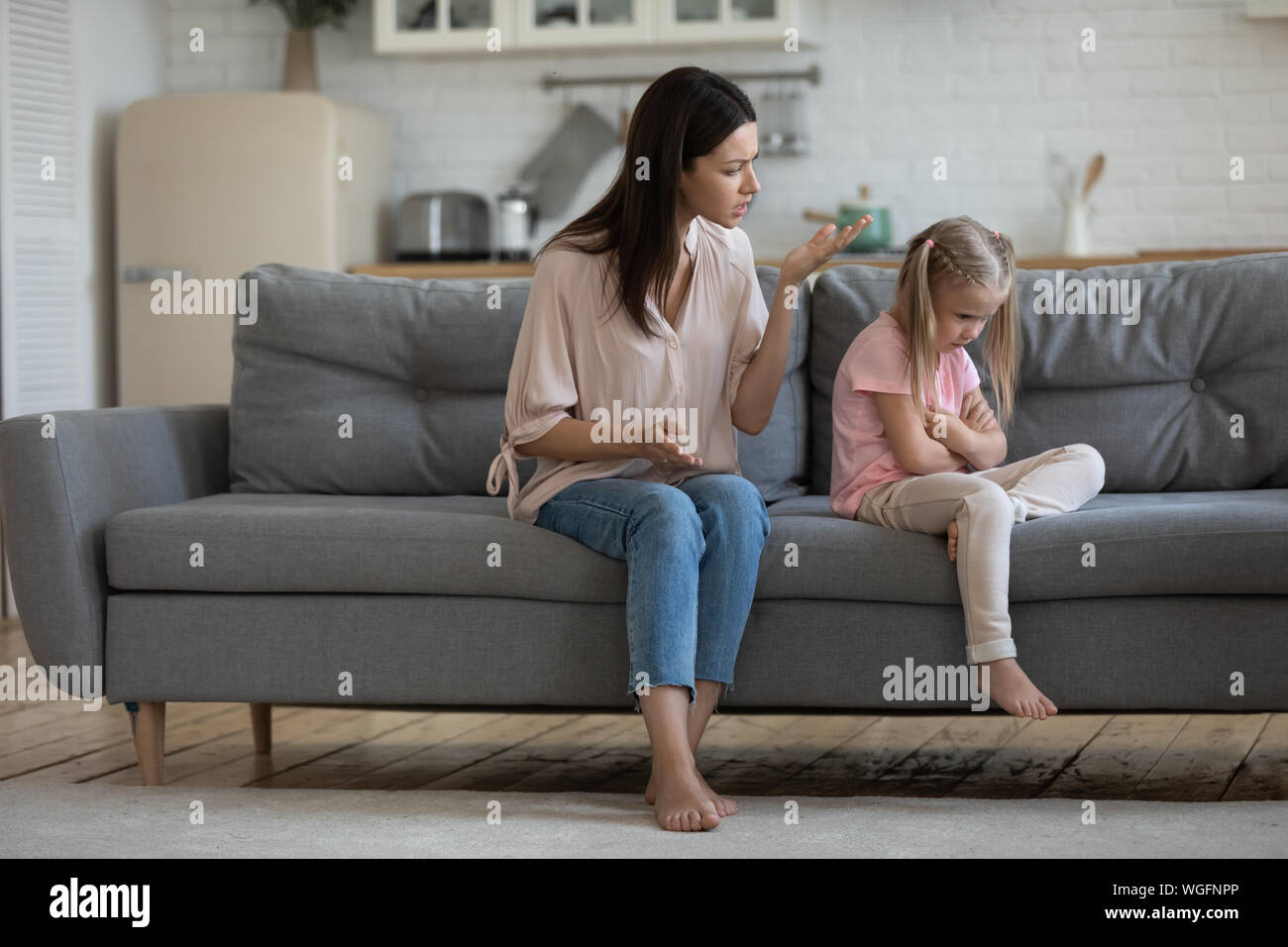 Mom scolds little daughter sitting on couch Stock Photo