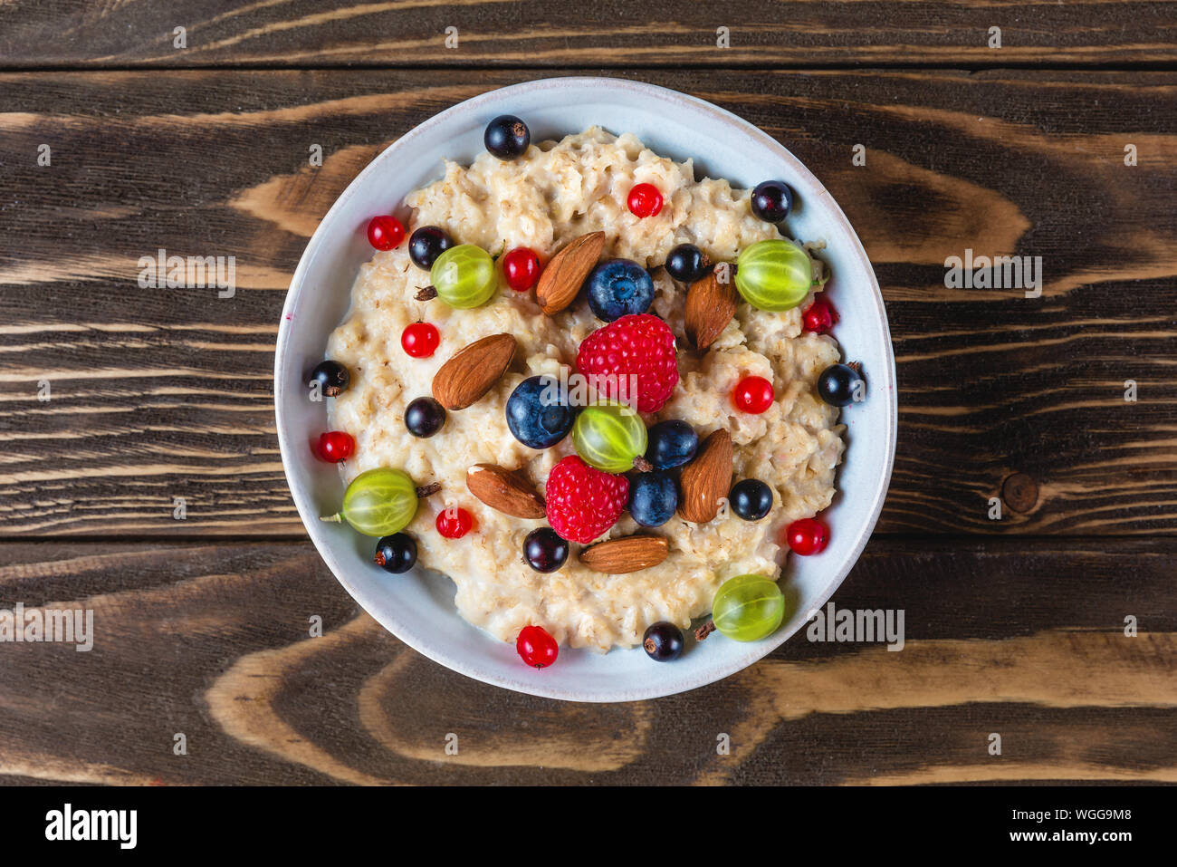 bowl of oatmeal porridge with fresh berries and nuts for healthy diet breakfast on rustic wooden table. top view Stock Photo
