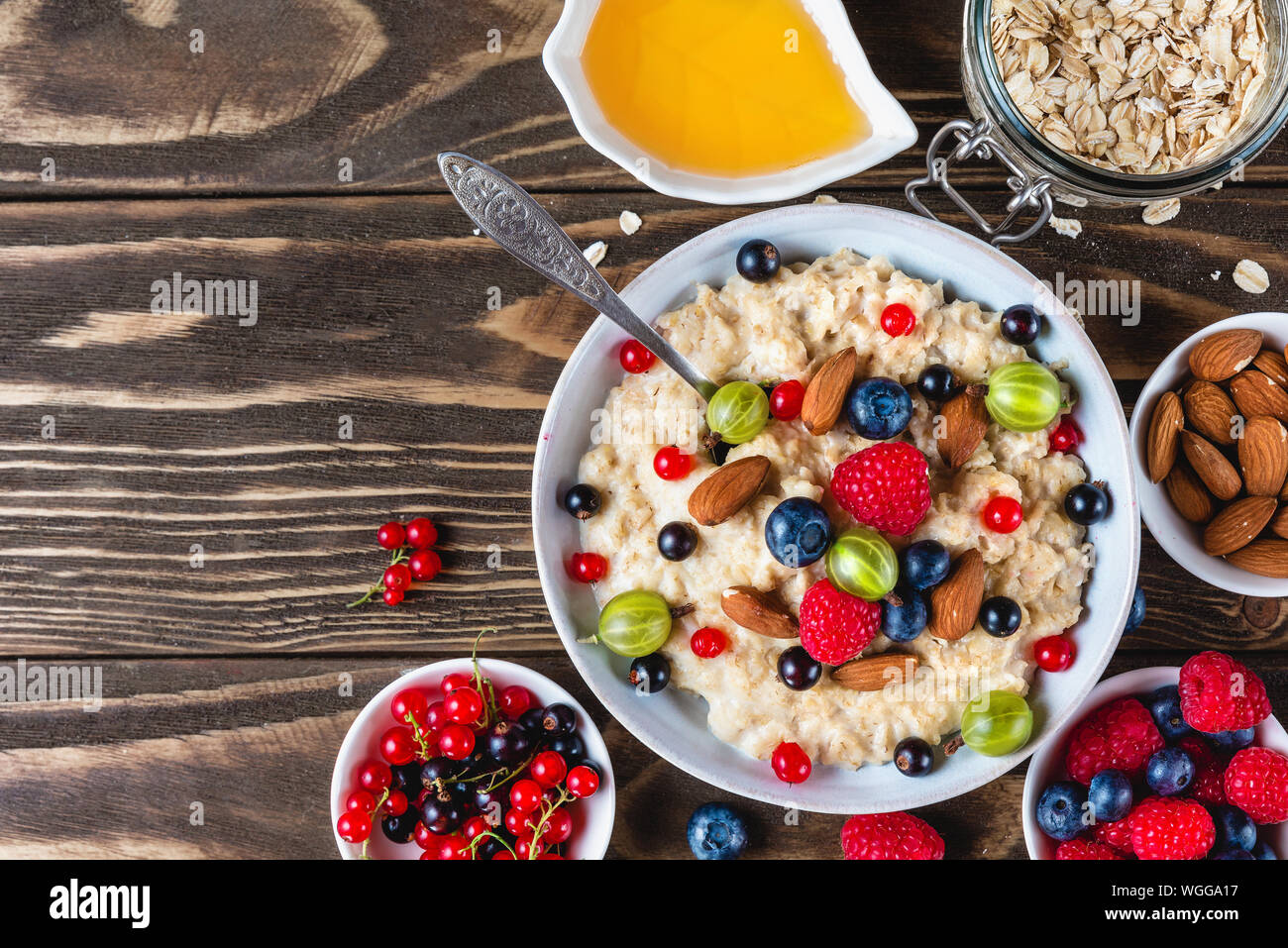 oatmeal porridge with fresh berries, honey and nuts in a bowl on rustic wooden background for healthy diet breakfast. top view with copy space Stock Photo
