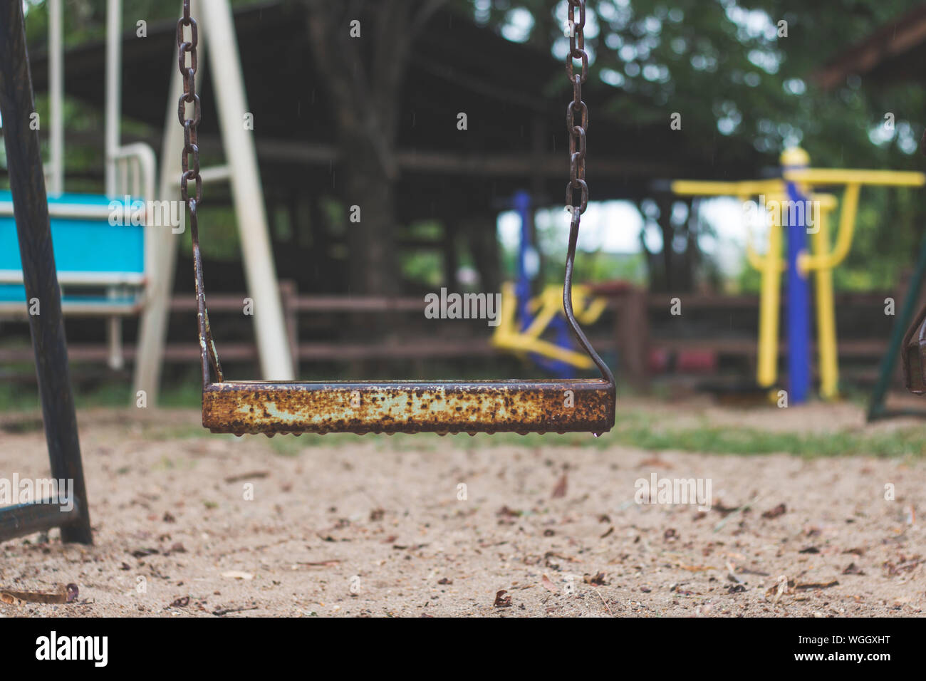 Wet Rusty Swing At Playground During Rainy Season Stock Photo