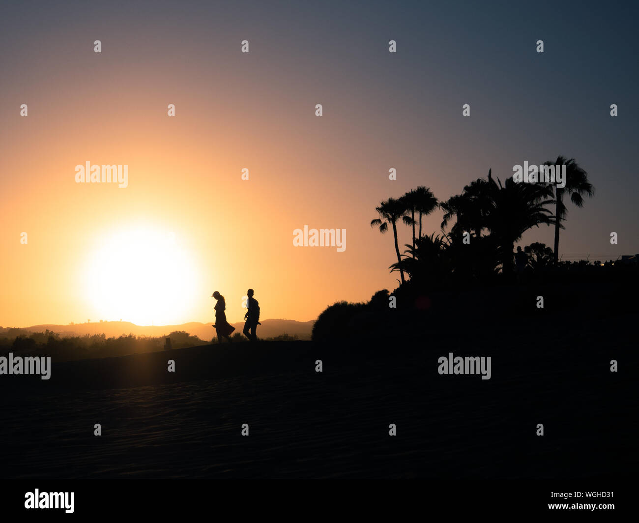 Silhouette of a couple walking from palm trees to the beach at sunset ...