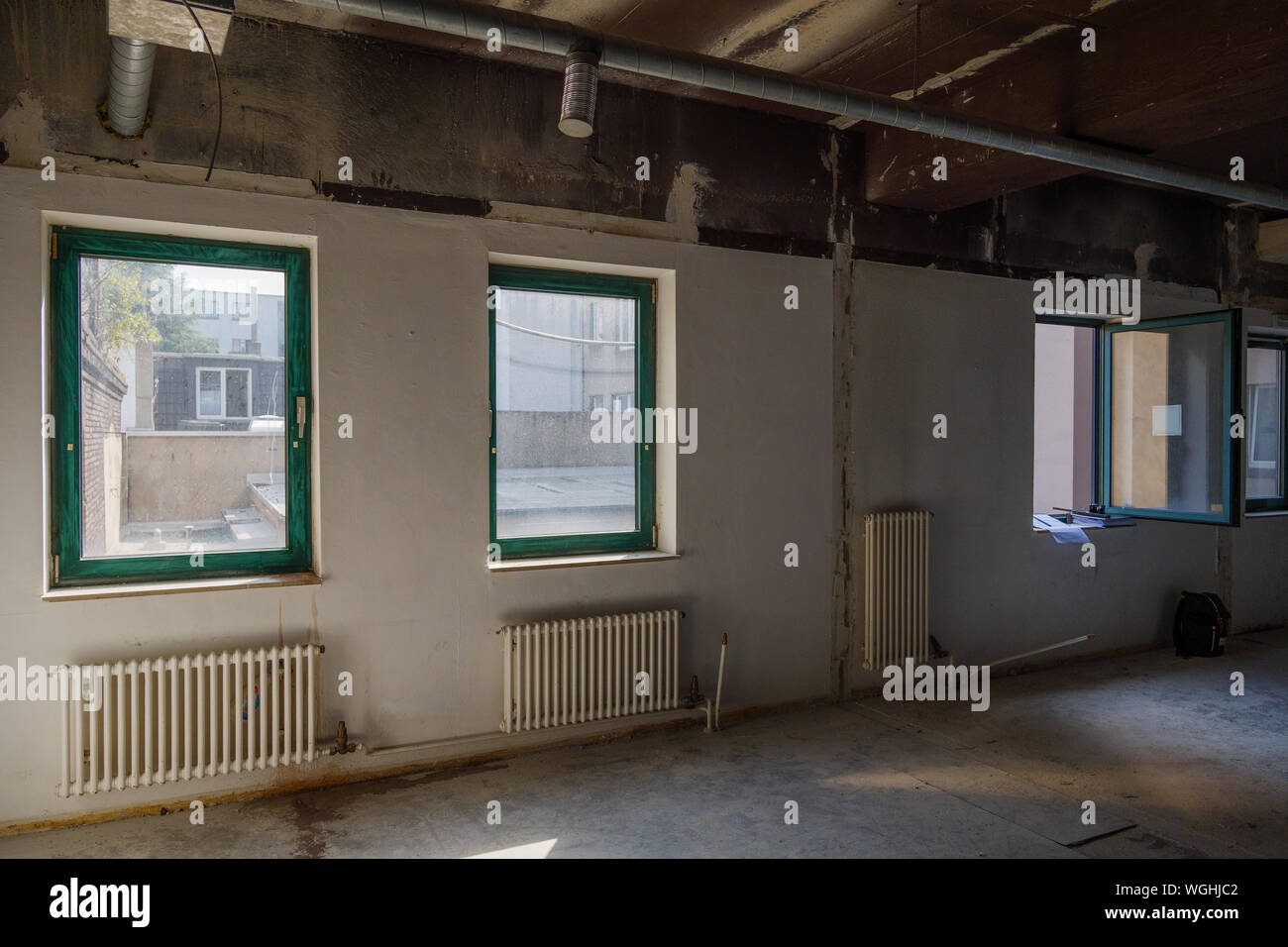 Interior view of empty abandon room with radiator heaters, glass windows and air duct system on ceiling. Stock Photo
