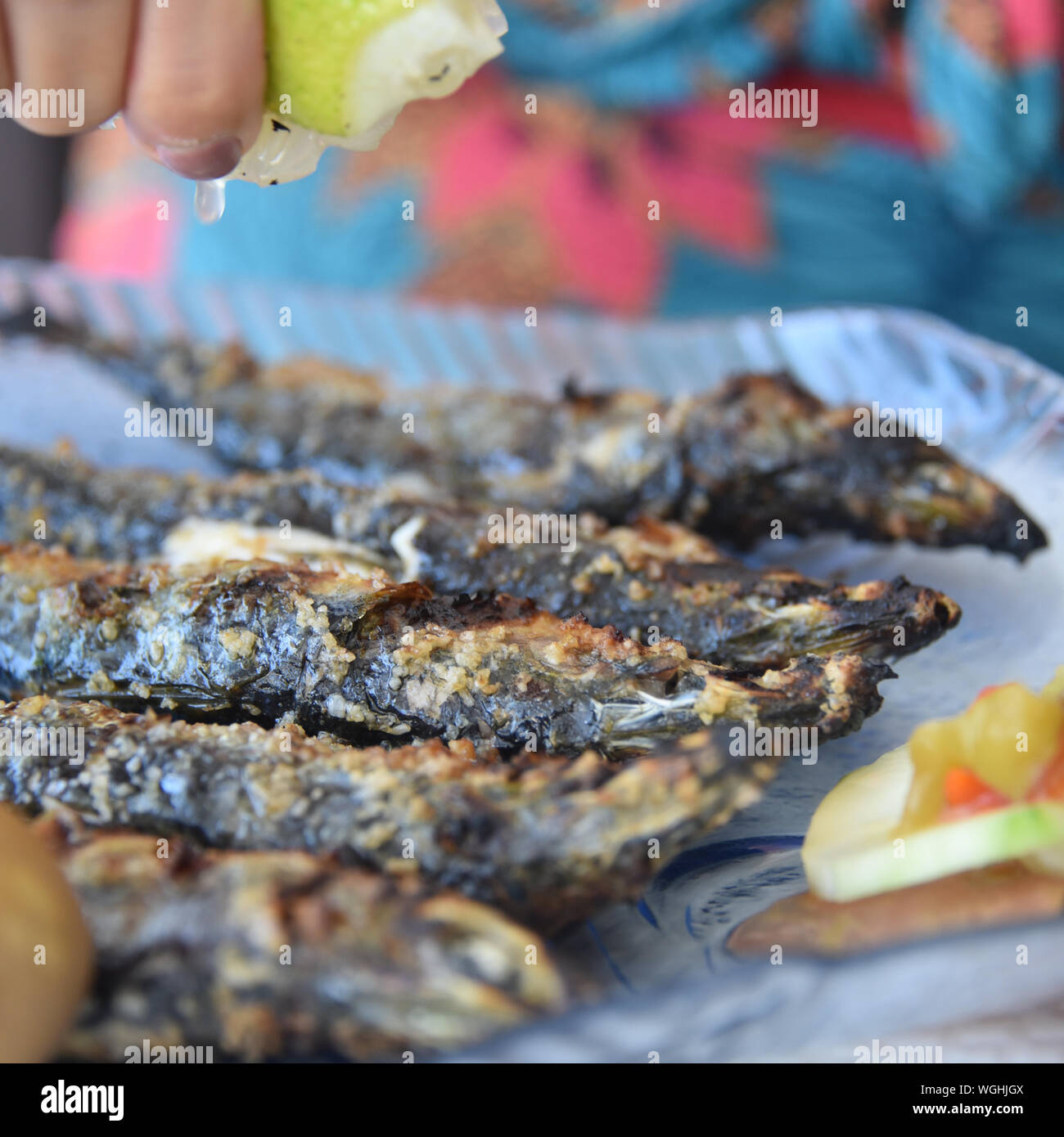 Lison, Portugal: A diner squeezes lemon juice onto freshly grilled Sardines Stock Photo