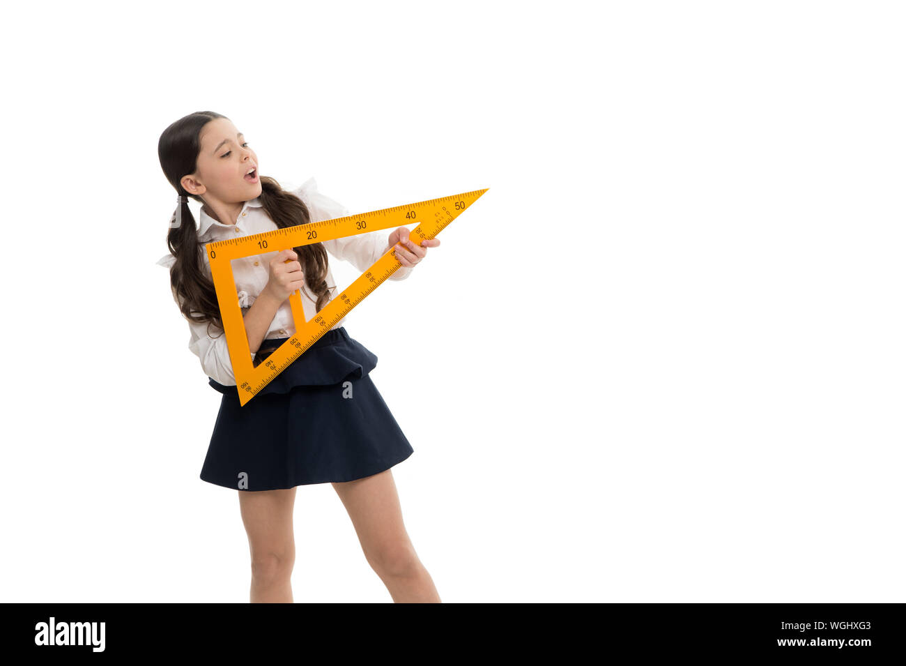 Education. Small child with measuring instrument at school lesson. Little girl preparing for geometry lesson. Cute schoolgirl hold triangular rulers for lesson. Stock Photo