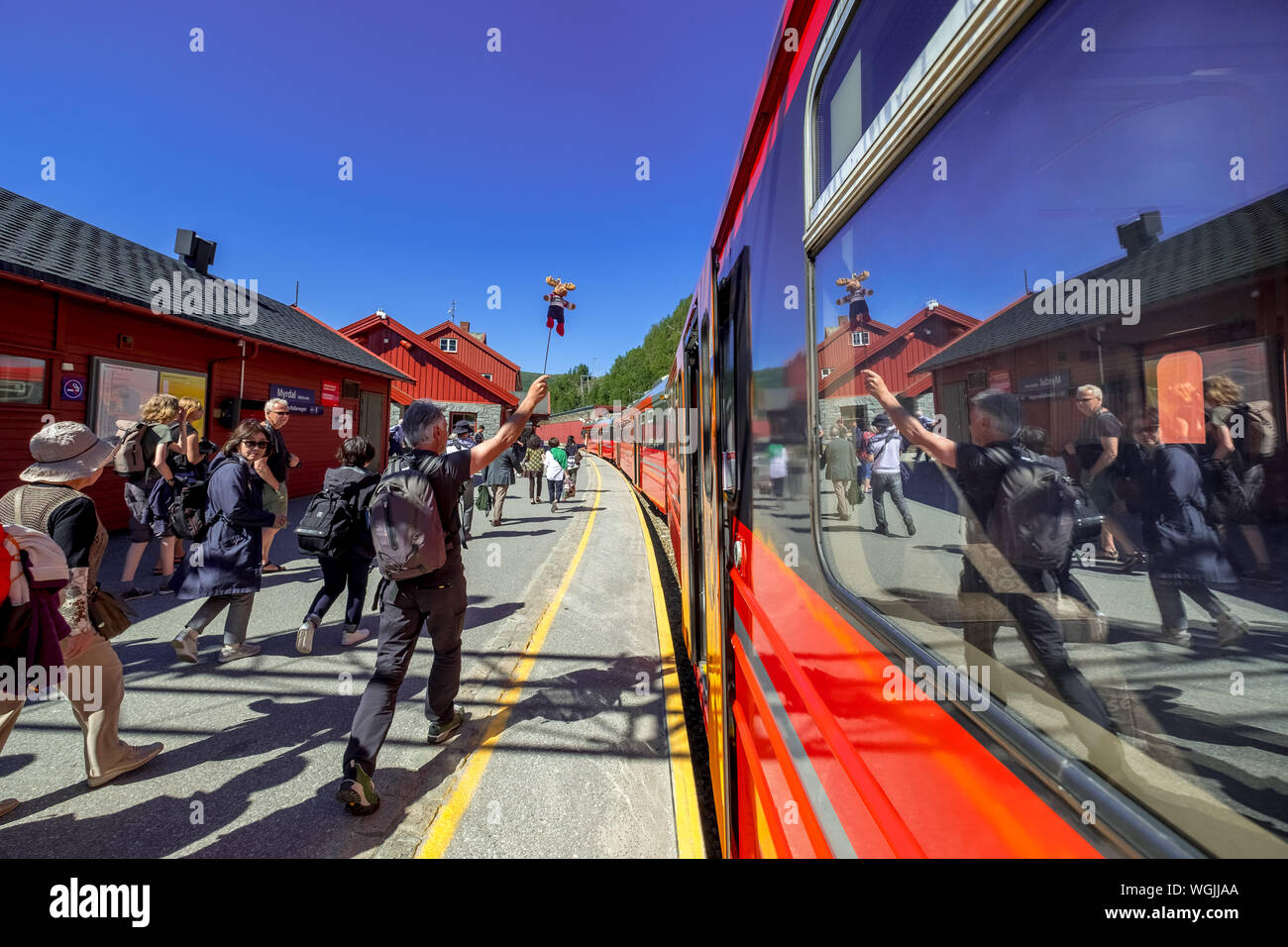 Tour guides are reflected in the train window, tourists on the platform, Bergensbahnen station, Myrdal, red wooden houses, red train, sky, Sogn og Fjo Stock Photo