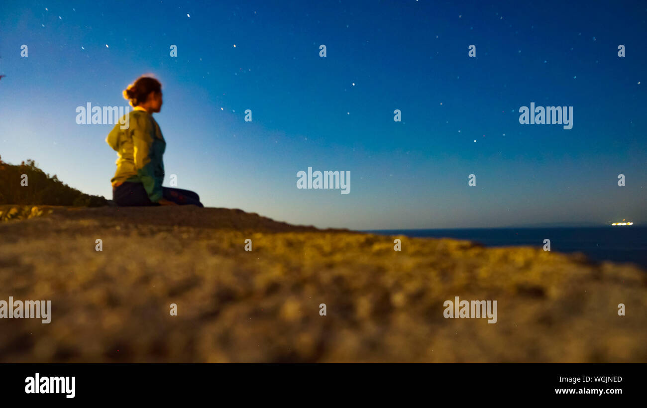 Young Woman Sitting Against Star Field At Beach Stock Photo