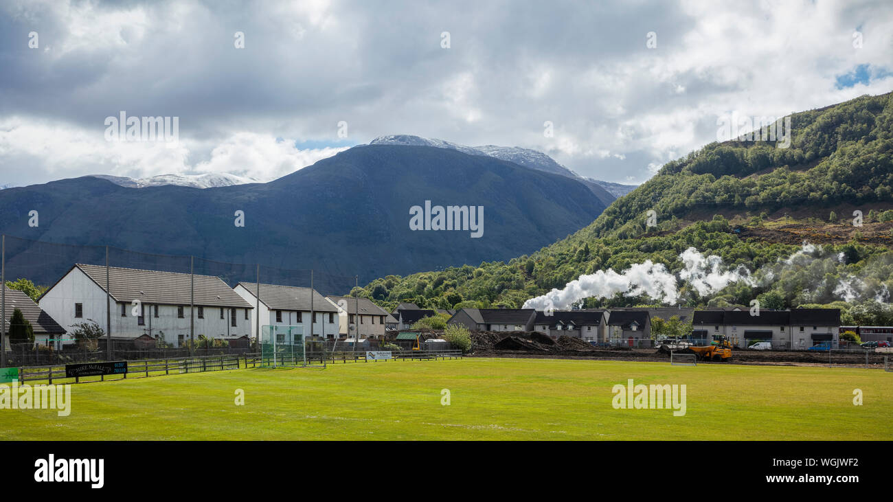 Jacobite steam train spouting steam as it leaves Fort William station in the West Highlands of Scotland with Ben Nevis in the distance Stock Photo