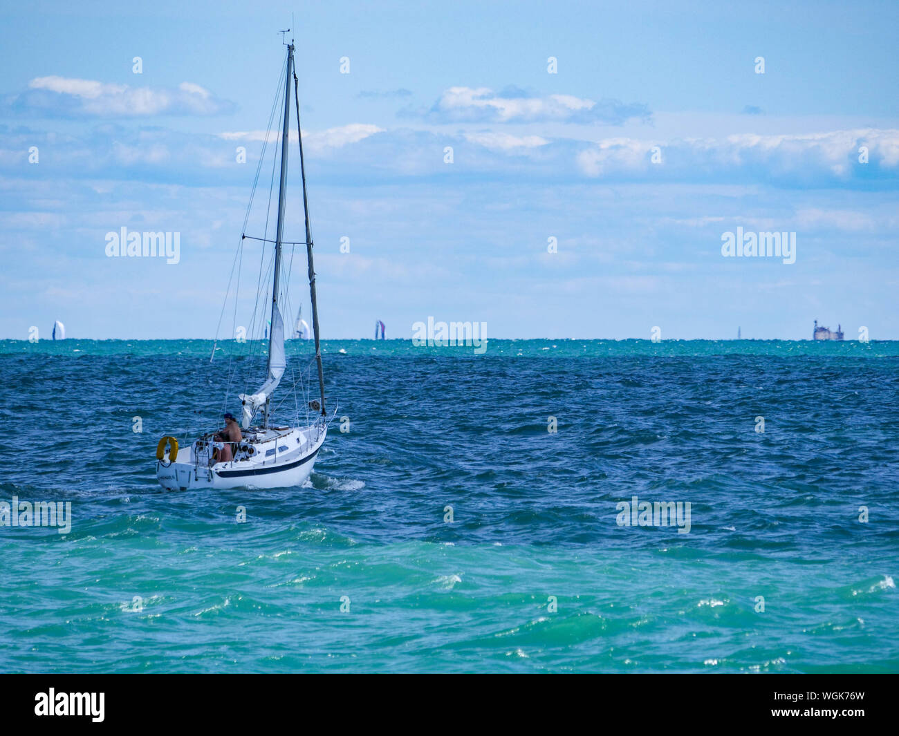 A sailboat navigating the choppy waters of Lake Michigan off Chicago. The masts of distant sailboats peek over the horizon in the distance. Stock Photo