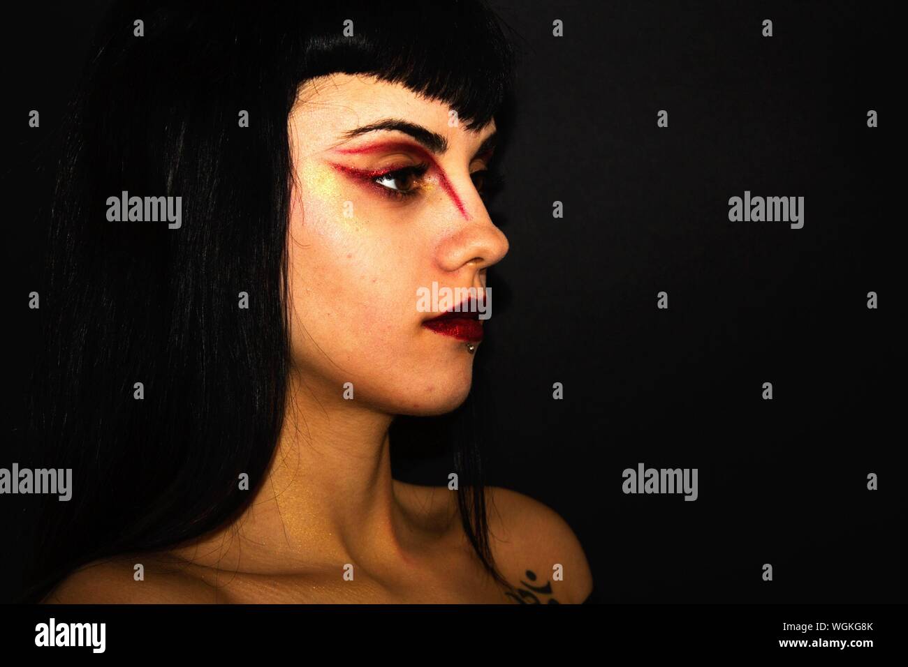 Close-up Of Woman With Red Eyeshadow Looking Away Against Black Background Stock Photo