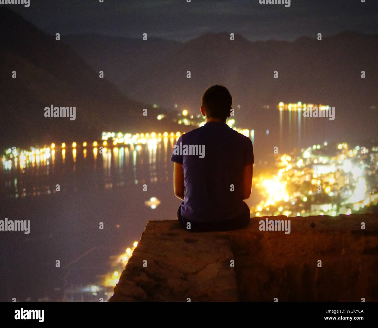 Rear View Of Man Sitting On Cliff Against Illuminated City At Night Stock Photo Alamy Rear View Of Man Sitting On Cliff Against Illuminated City At Night Stock Photo Alamy