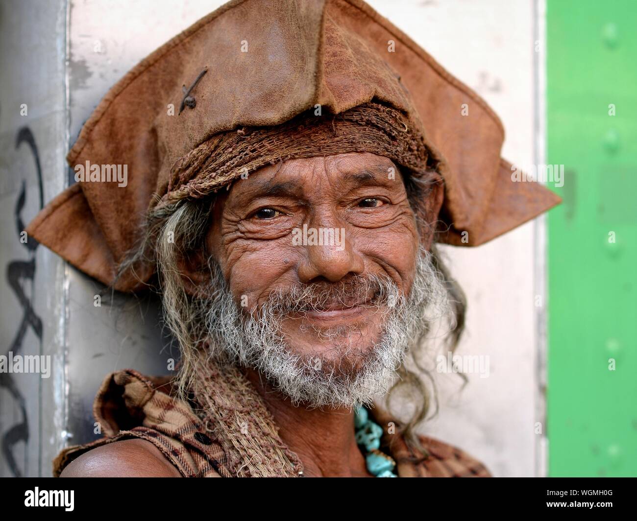 Rugged elderly man wears a worn brown Jack Sparrow tricorn hat and smiles for the camera. Stock Photo