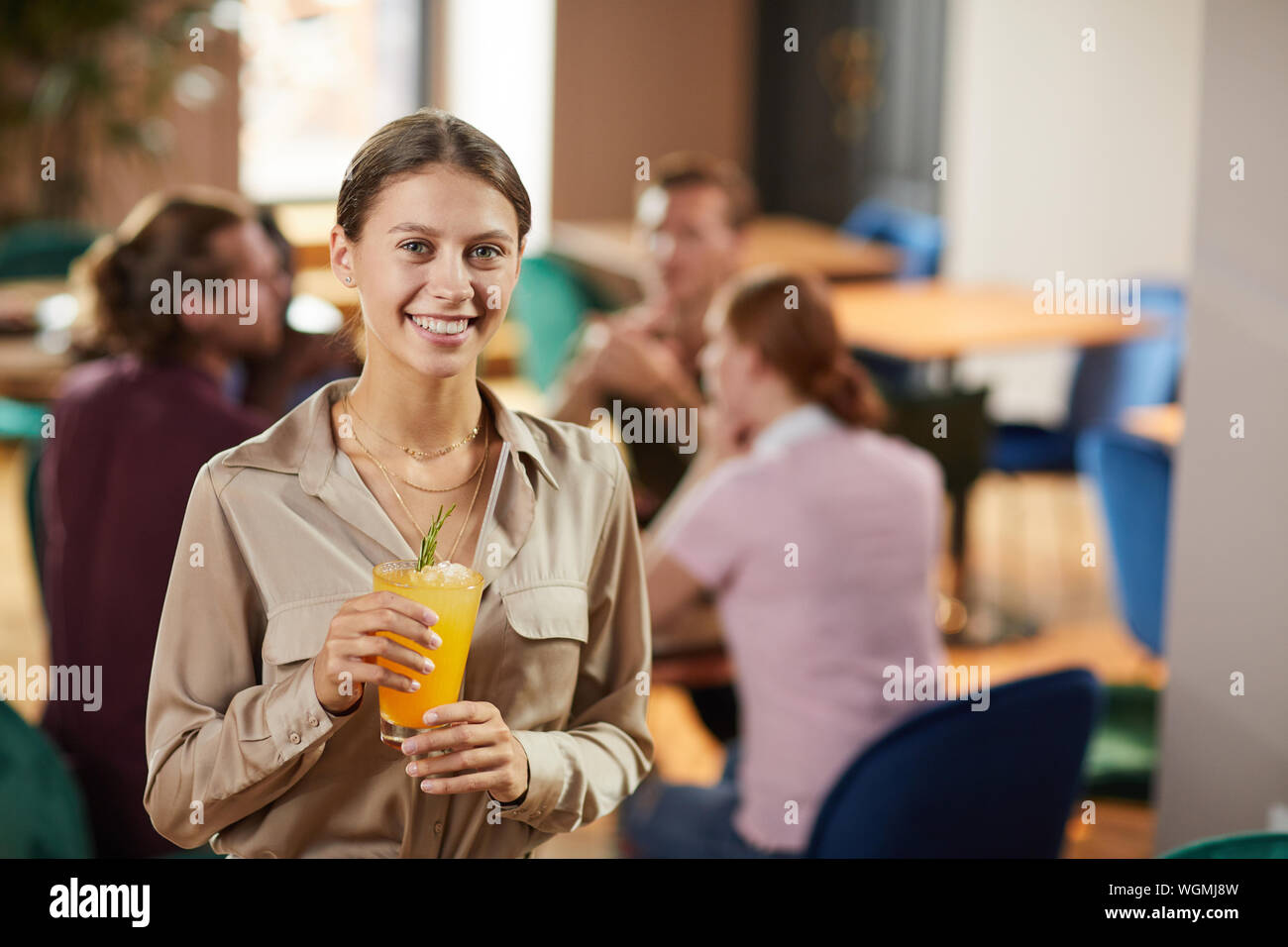 Waist up portrait of cheerful young woman looking at camera while holding refreshing drink in cafe, copy space Stock Photo