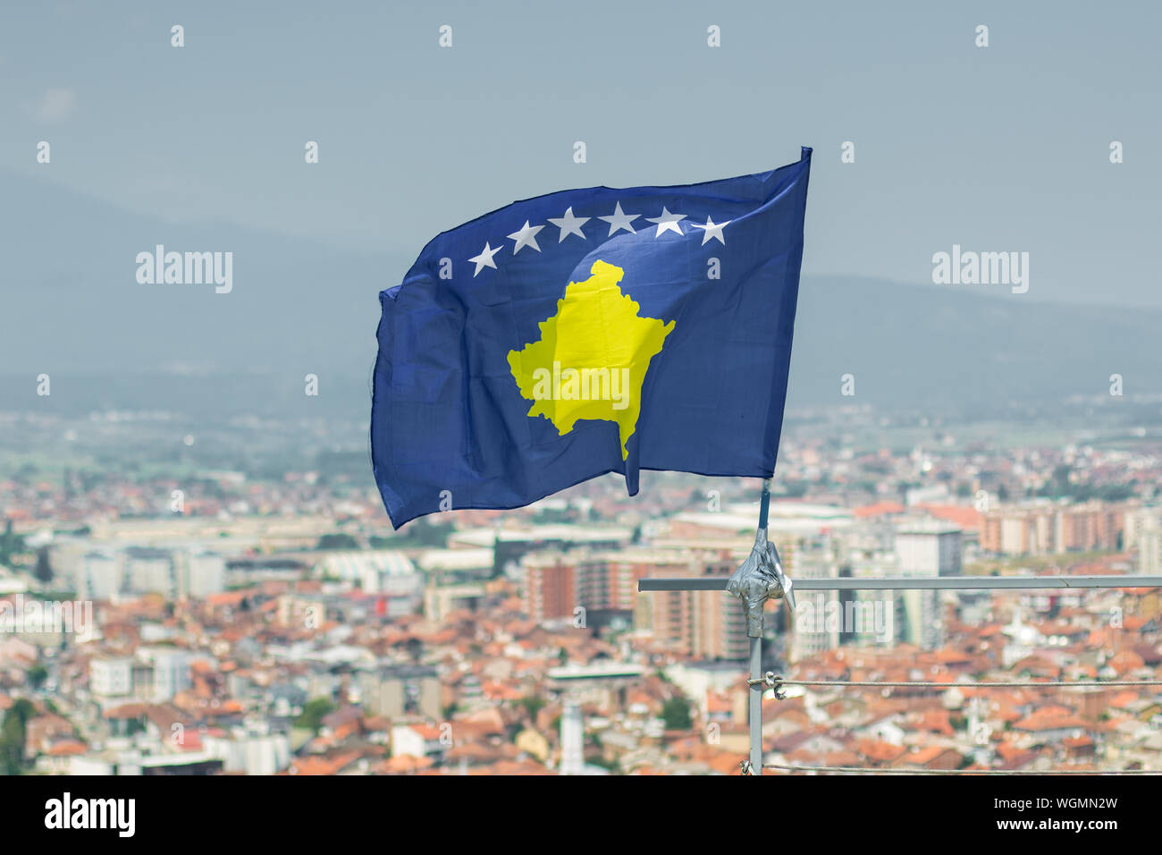 waving flag of Kosovo in front of blurred city Stock Photo