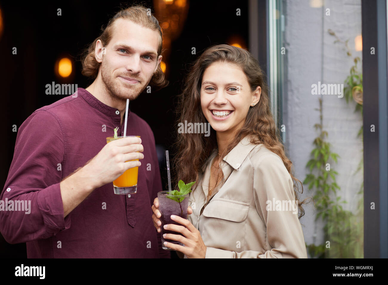 Waist up portrait of beautiful young couple drinking cocktails while posing outdoors standing by cafe, copy space Stock Photo