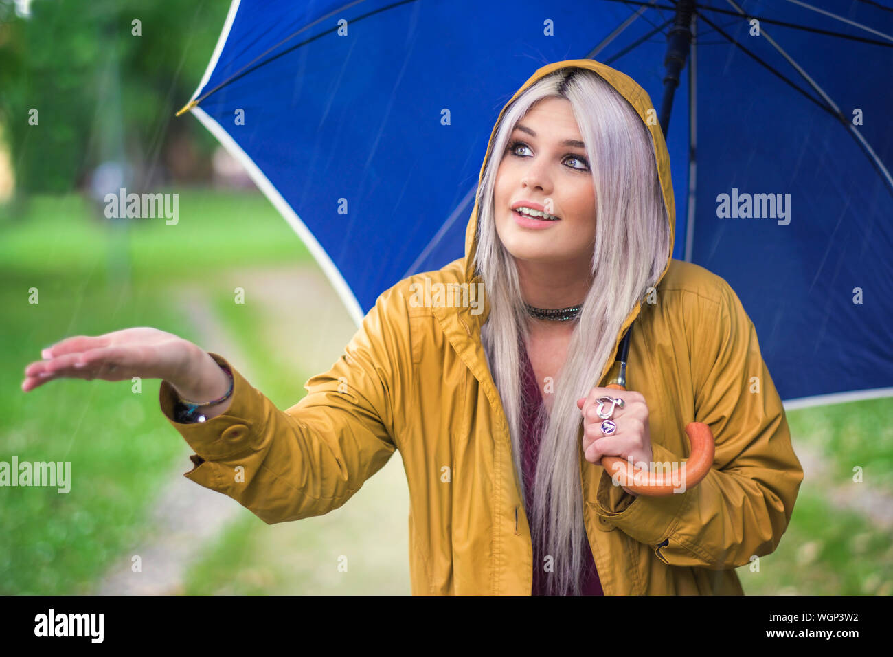 Young Woman With Blue Umbrella Enjoying Rain On Field Stock Photo