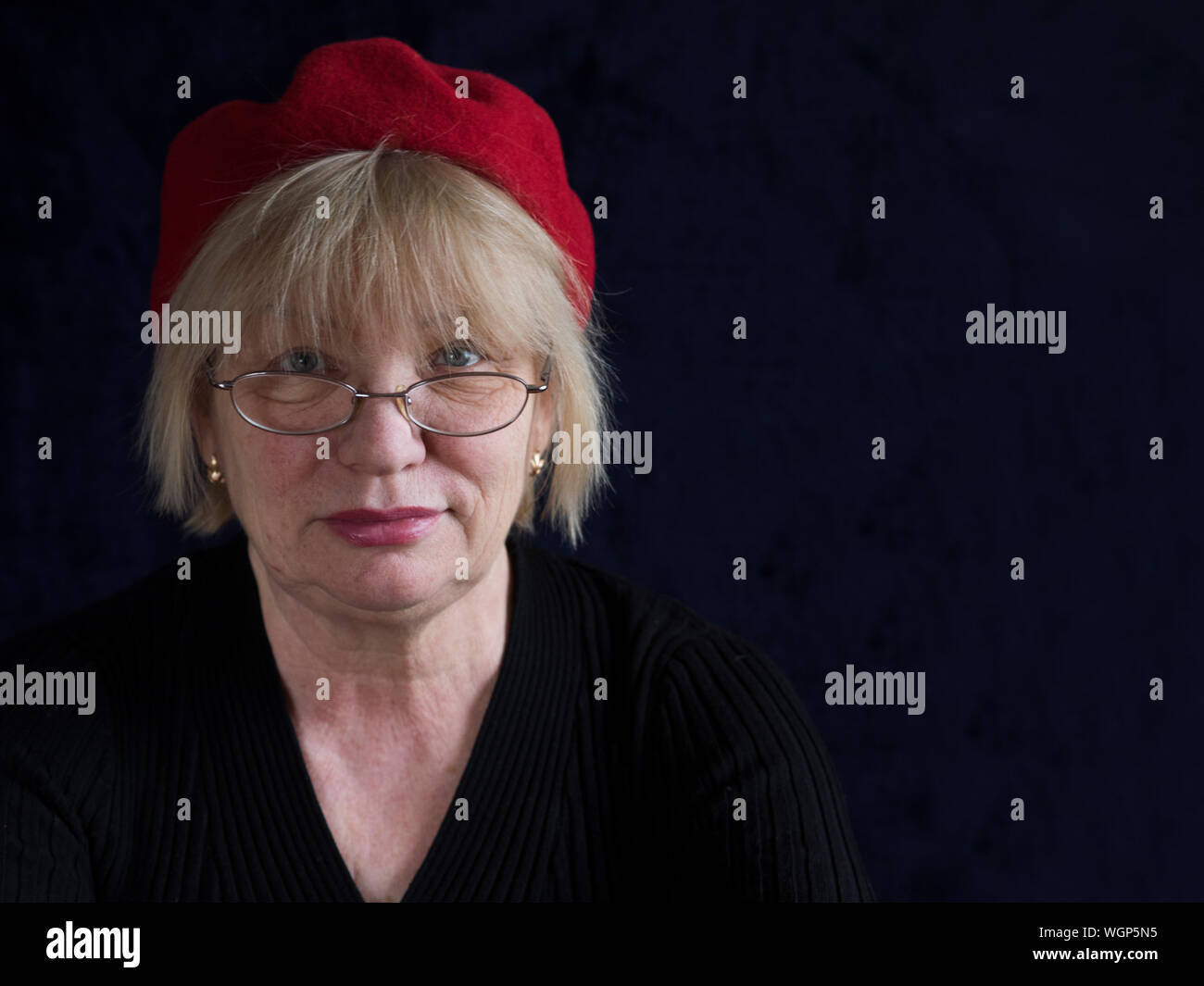 Portrait Of Mature Woman With Red Cap Against Black Background Stock Photo