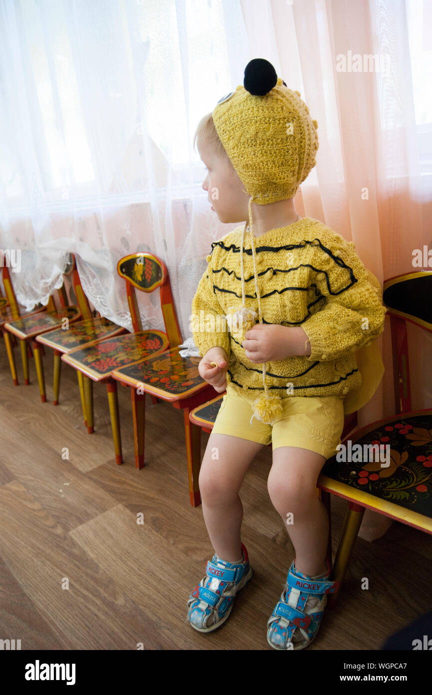 A three-year-old child, a sad blond boy with blue eyes, in a bee costume made by his parents at a matinee in kindergarten, yellow knitwear, a knitted jumper, a hat, black ears and horns Stock Photo