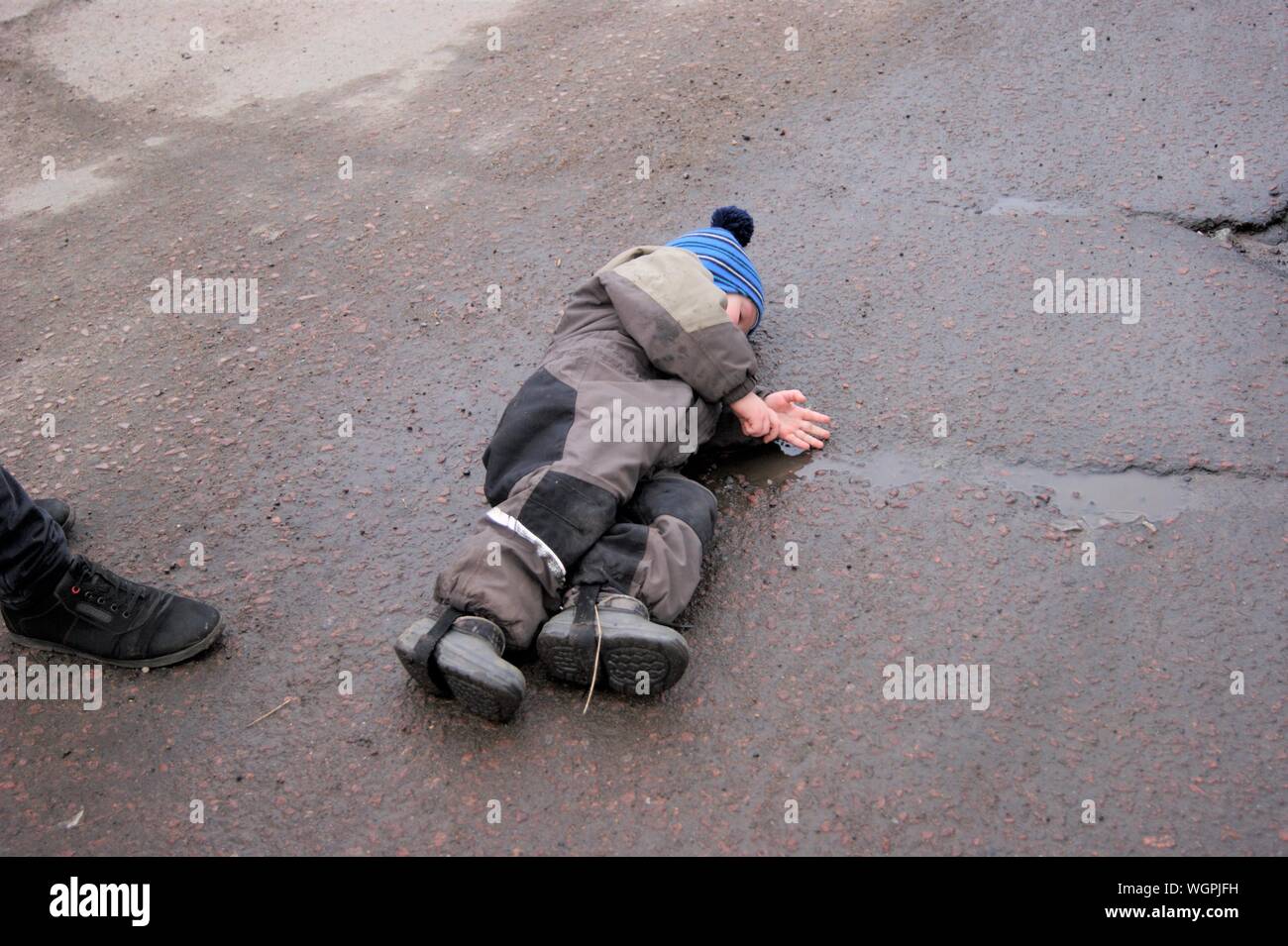 Children's caprice - a little boy lay down on the asphalt to express his protest and disagreement with the parent Stock Photo