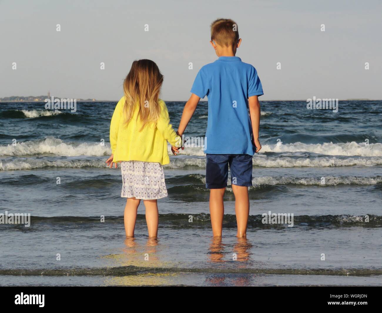 Rear View Of Siblings Holding Hands While Standing On Shore Stock Photo ...