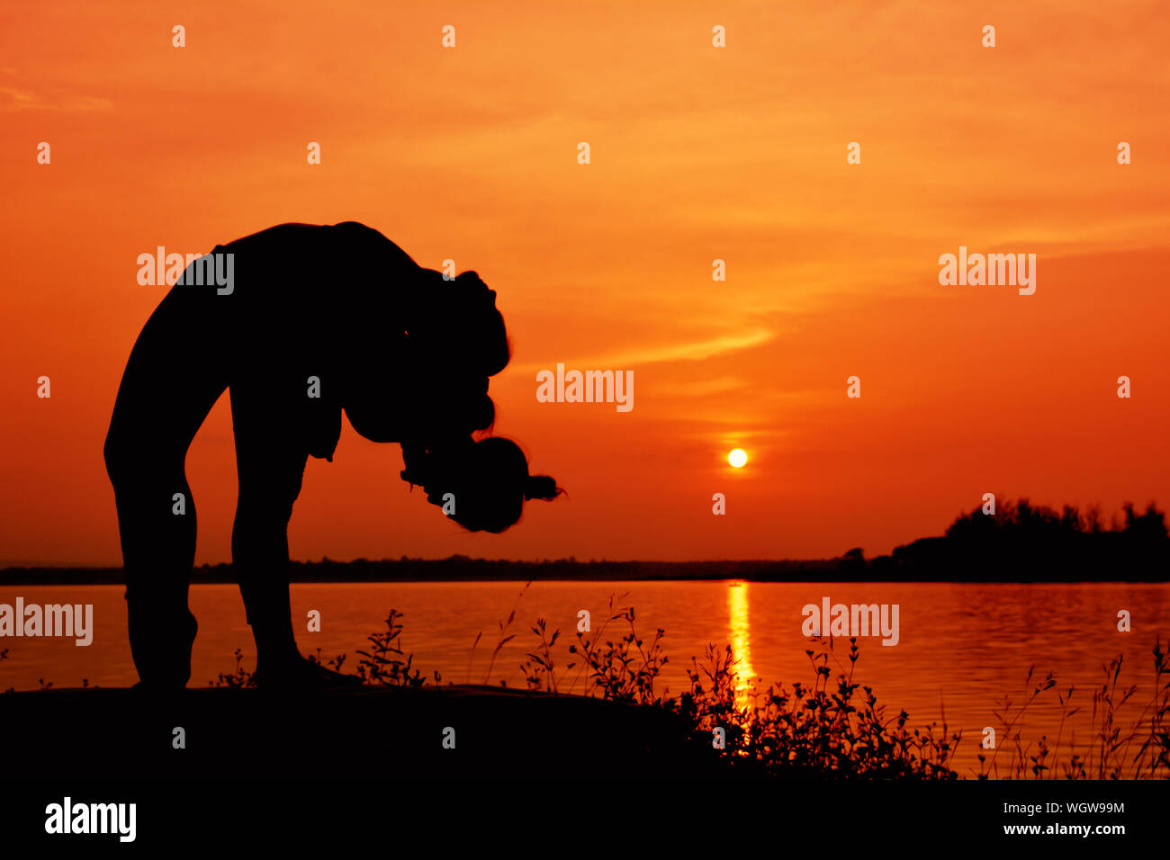 Silhouette Person Bending While Standing At Lakeshore During Sunset Stock Photo