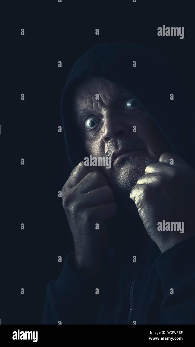 Close-up Of Frightened Man Wearing Hood Against Black Background Stock Photo