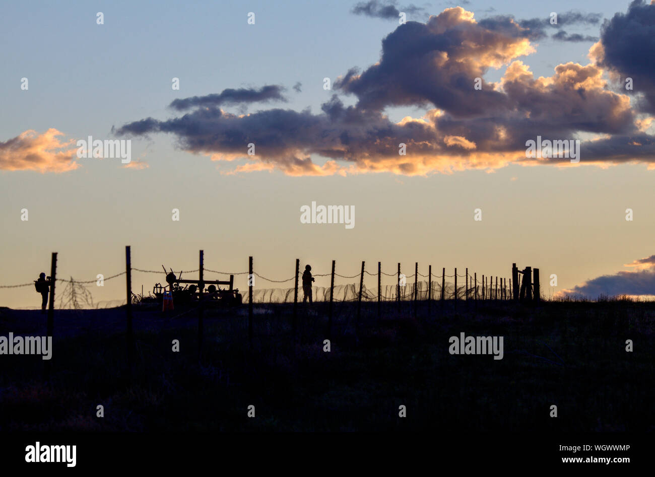 Two silhouetted photographers stand behind a farm fence photographing a Colorado sunset. Stock Photo