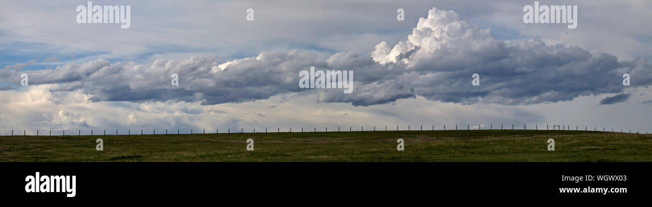 A lonely fence stretches across the lone prairie with a backdrop of late afternoon sunlit clouds. Stock Photo