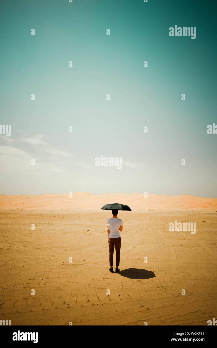 Rear View Of Man Standing In Desert With Umbrella Stock Photo