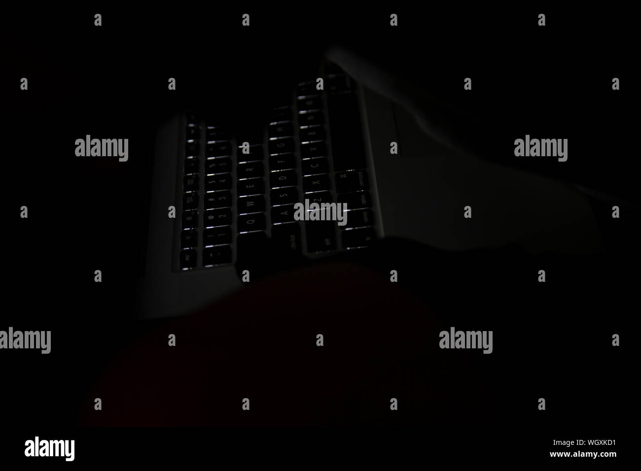 Partially obstructed laptop keyboard with keys glowing in the dark