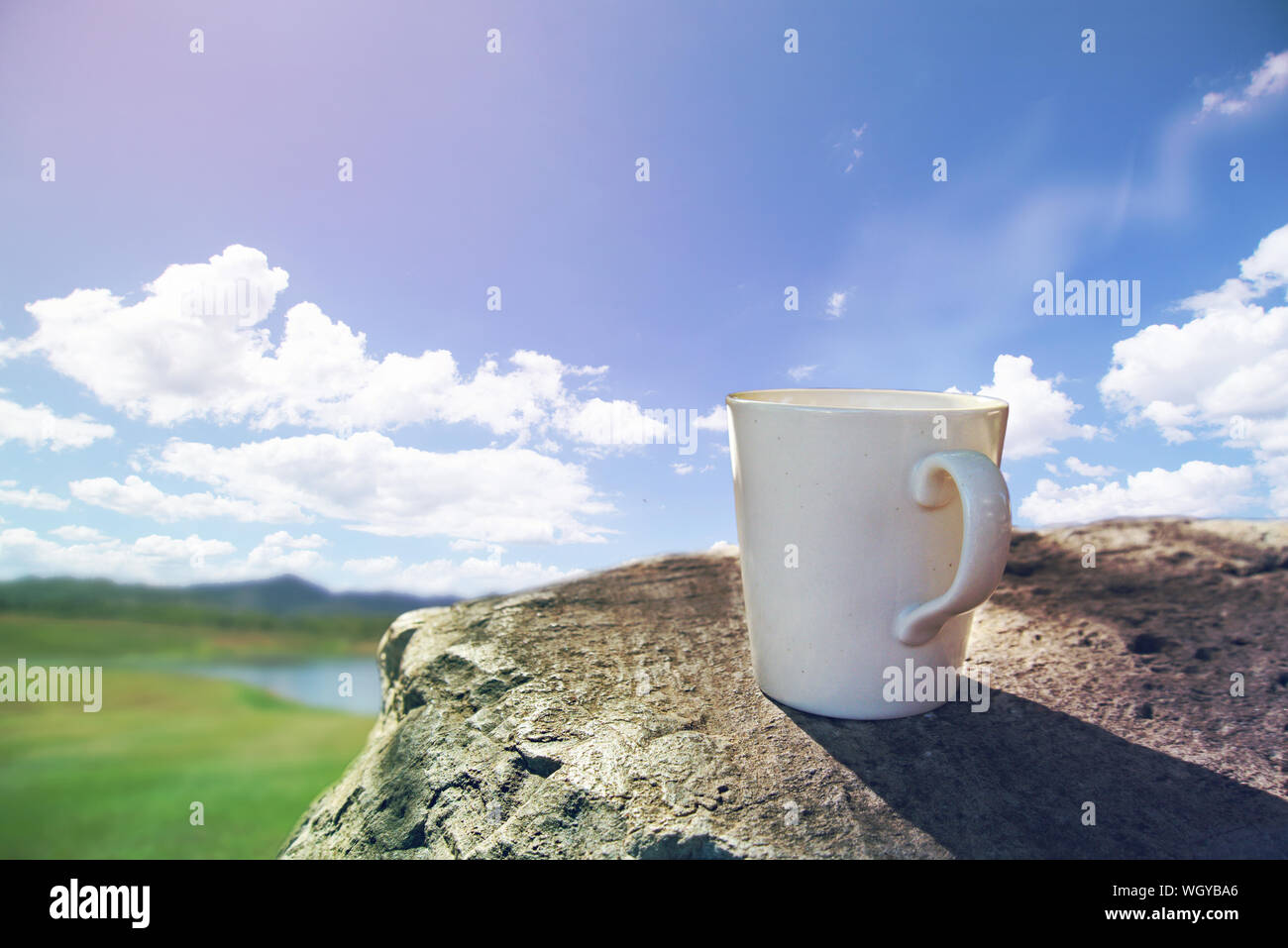 In the morning, a coffee cup placed on the stone bench with soft sunlight and blue sky background. Stock Photo