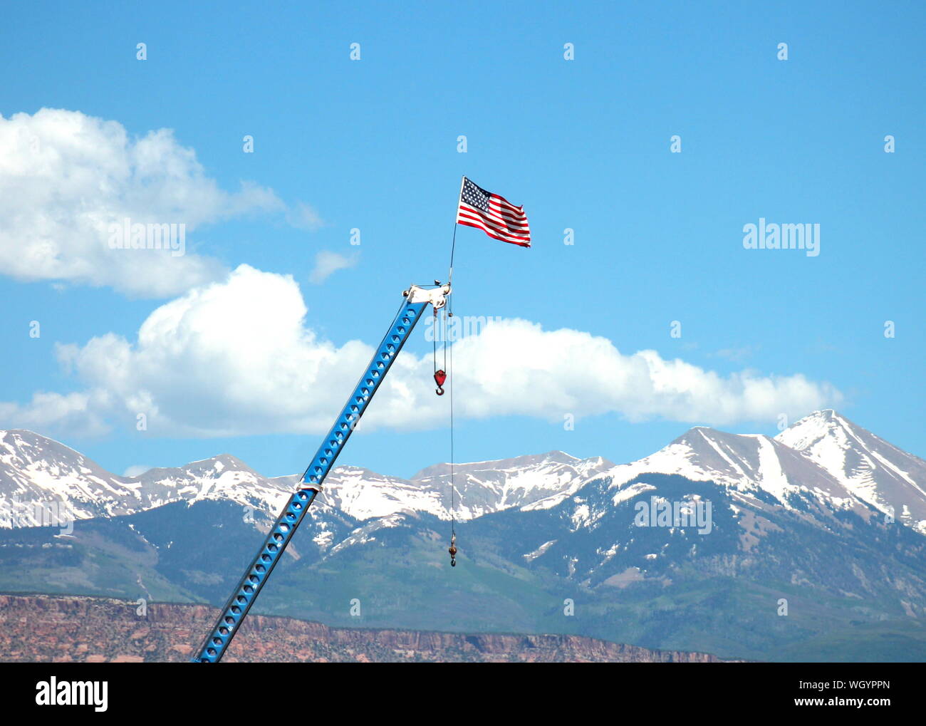 American Flag Waving On Crane Against Snowcapped Mountains Stock Photo
