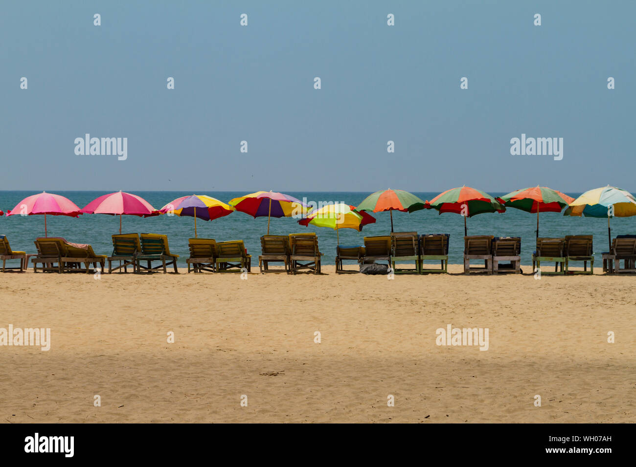 Row of covered wooden sun beds with colorful umbrellas on the beach in
