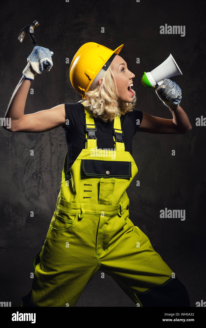Female Construction Worker Shouting On Megaphone While Standing Against Wall Stock Photo