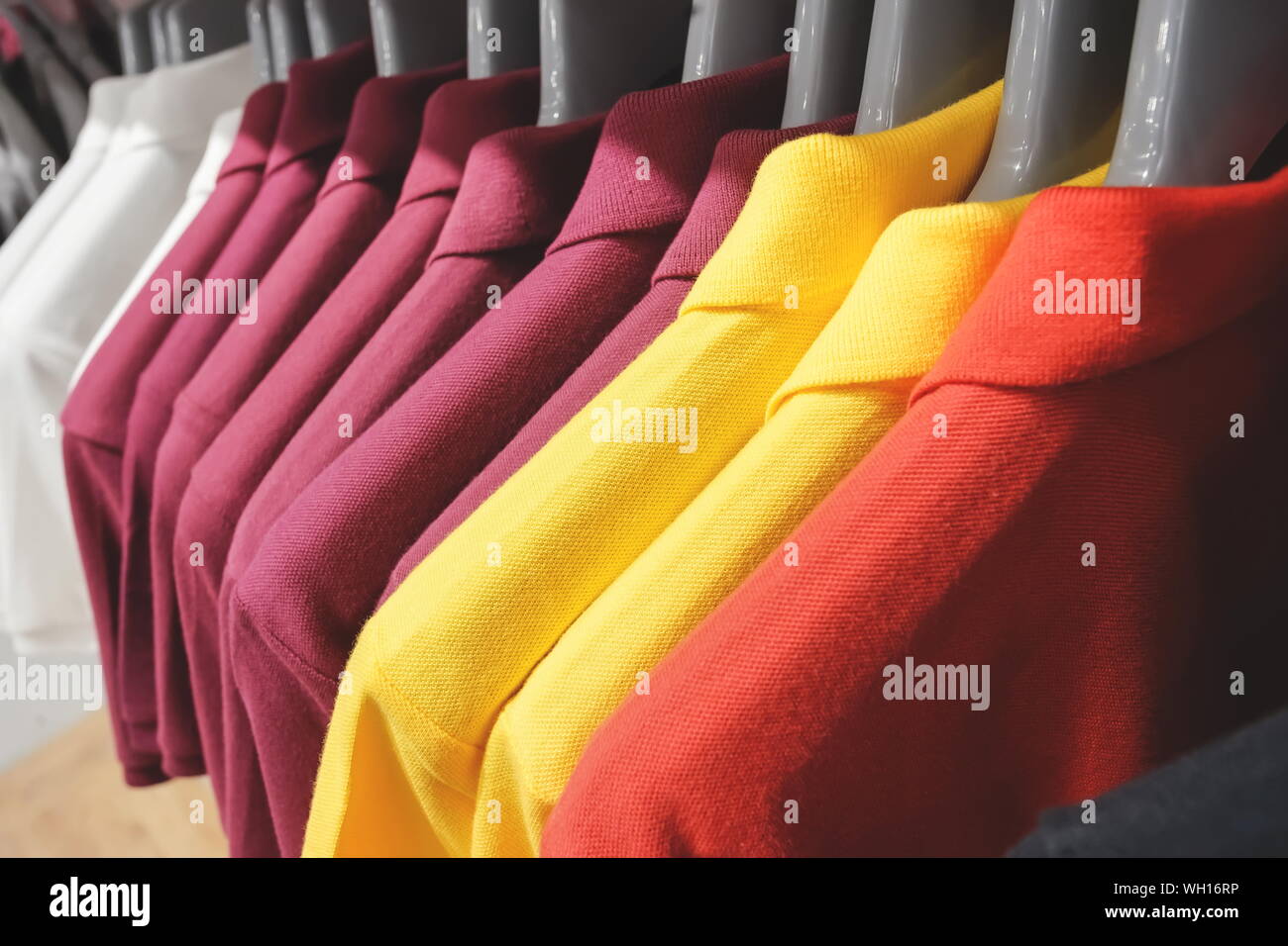 Closed up hanging red, yellow, dark purple and white polo shirts. Stock Photo