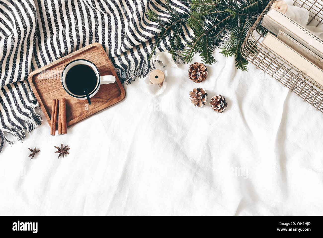 Christmas styled composition. Cup of coffee, plaid, old books in golden basket, pine cones, fir branches on white table, linen background. Flat lay, t Stock Photo