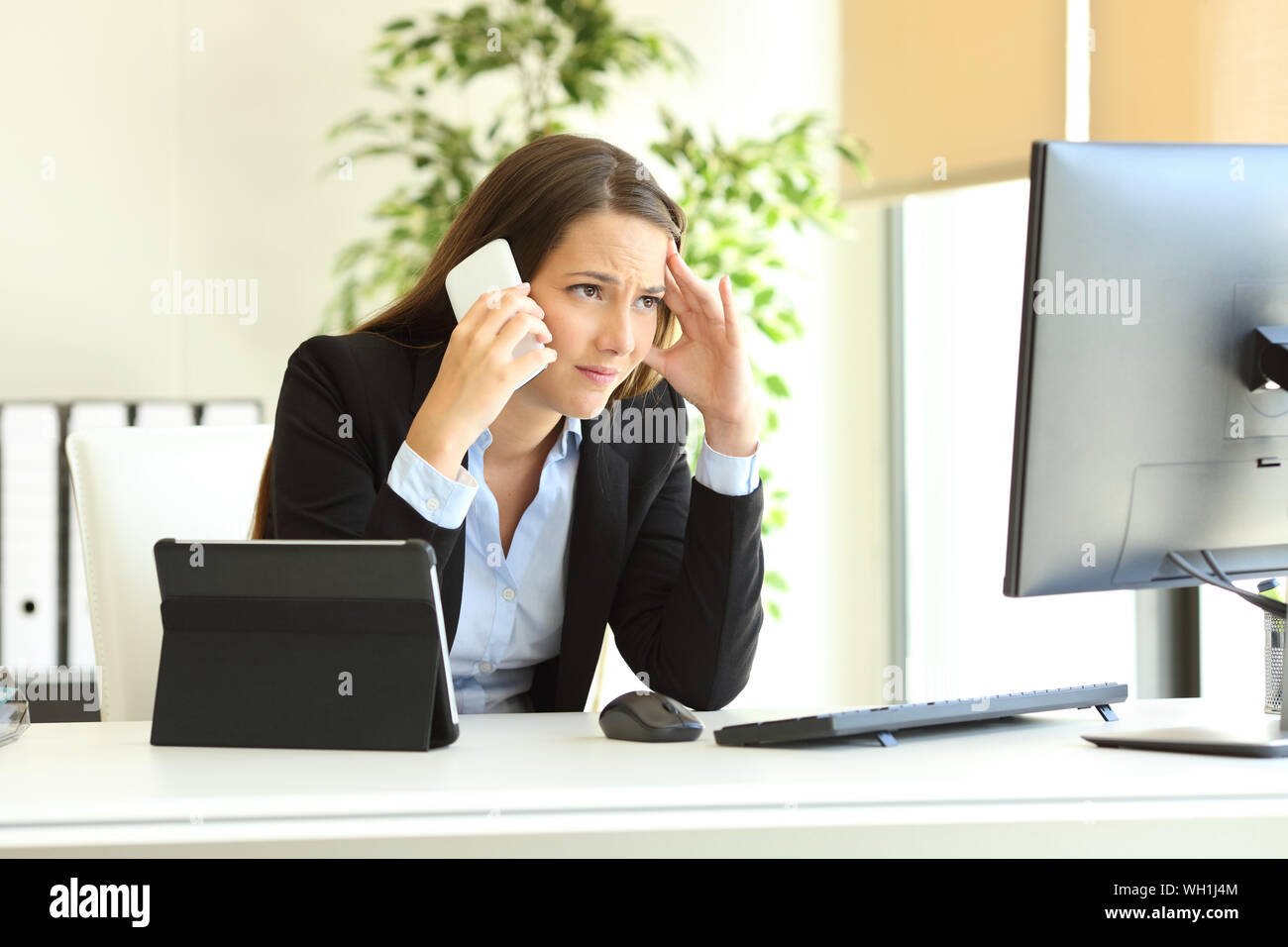 Worried office worker using multiple devices calling on phone at workplece Stock Photo