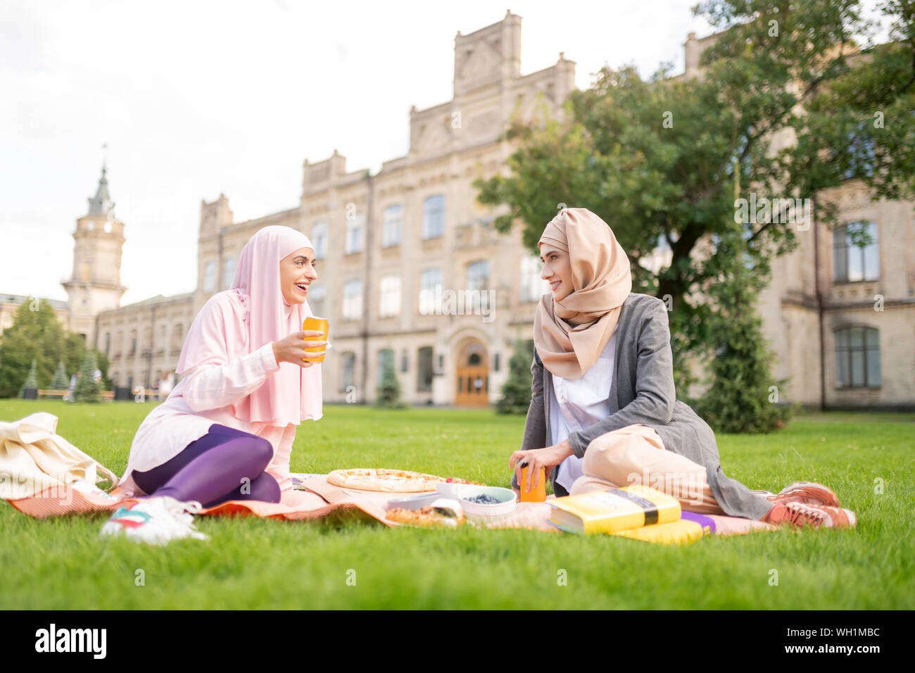 Muslim students eating and drinking while sitting on lawn Stock Photo