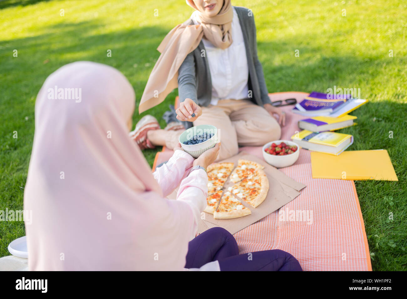 Women in hijab taking blueberries after studying with friend Stock Photo