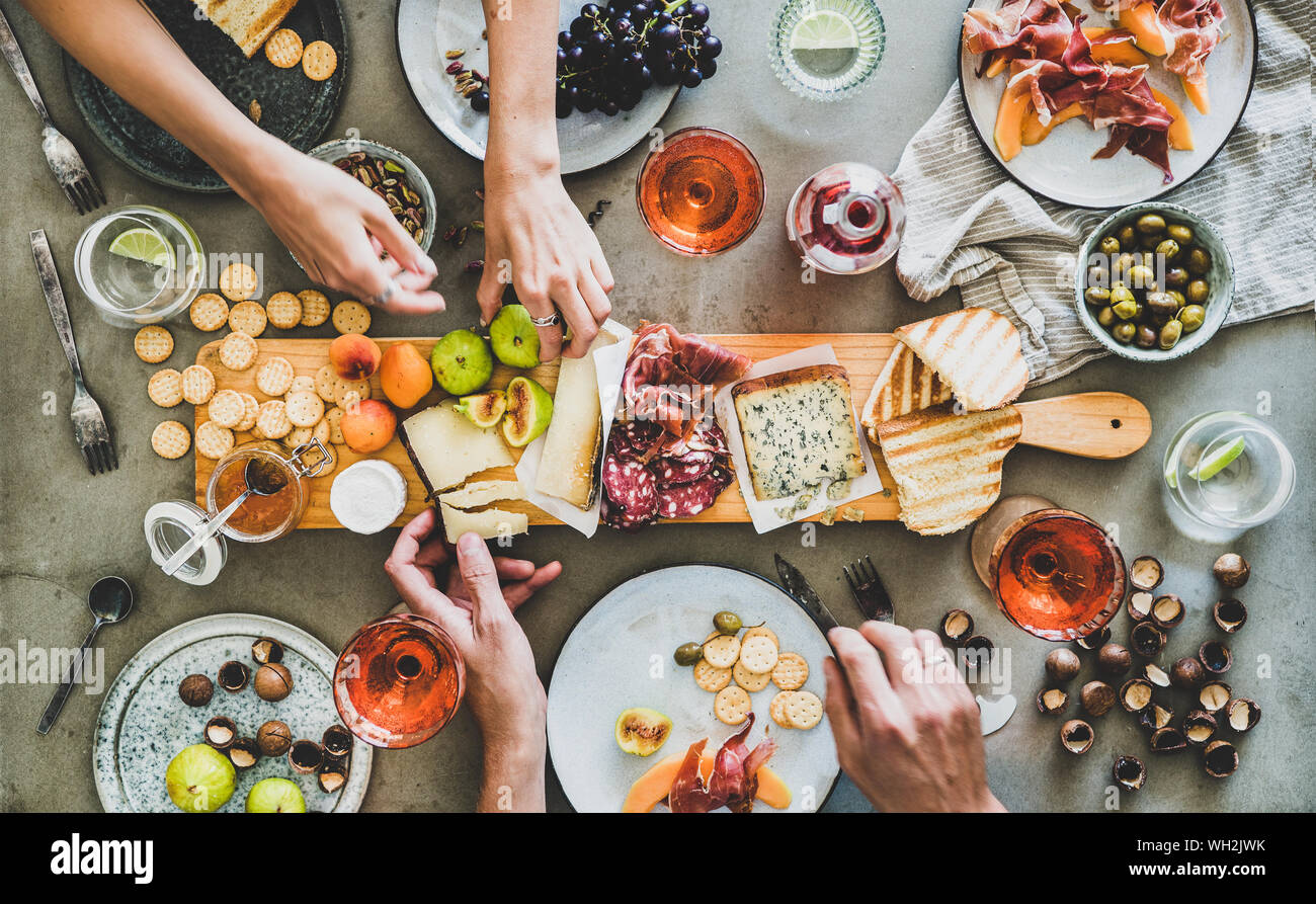 Mid-summer picnic with wine and snacks. Flat-lay of charcuterie and cheese  board, rose wine, nuts, olives and peoples hands over concrete table backgr  Stock Photo - Alamy