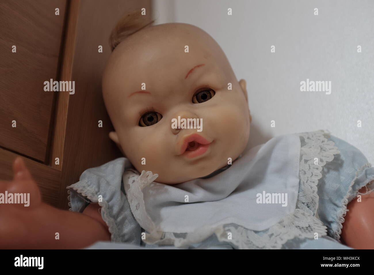 Old, worn and grimy toy doll with an eerie look, sitting in the corner of a room. Stock Photo