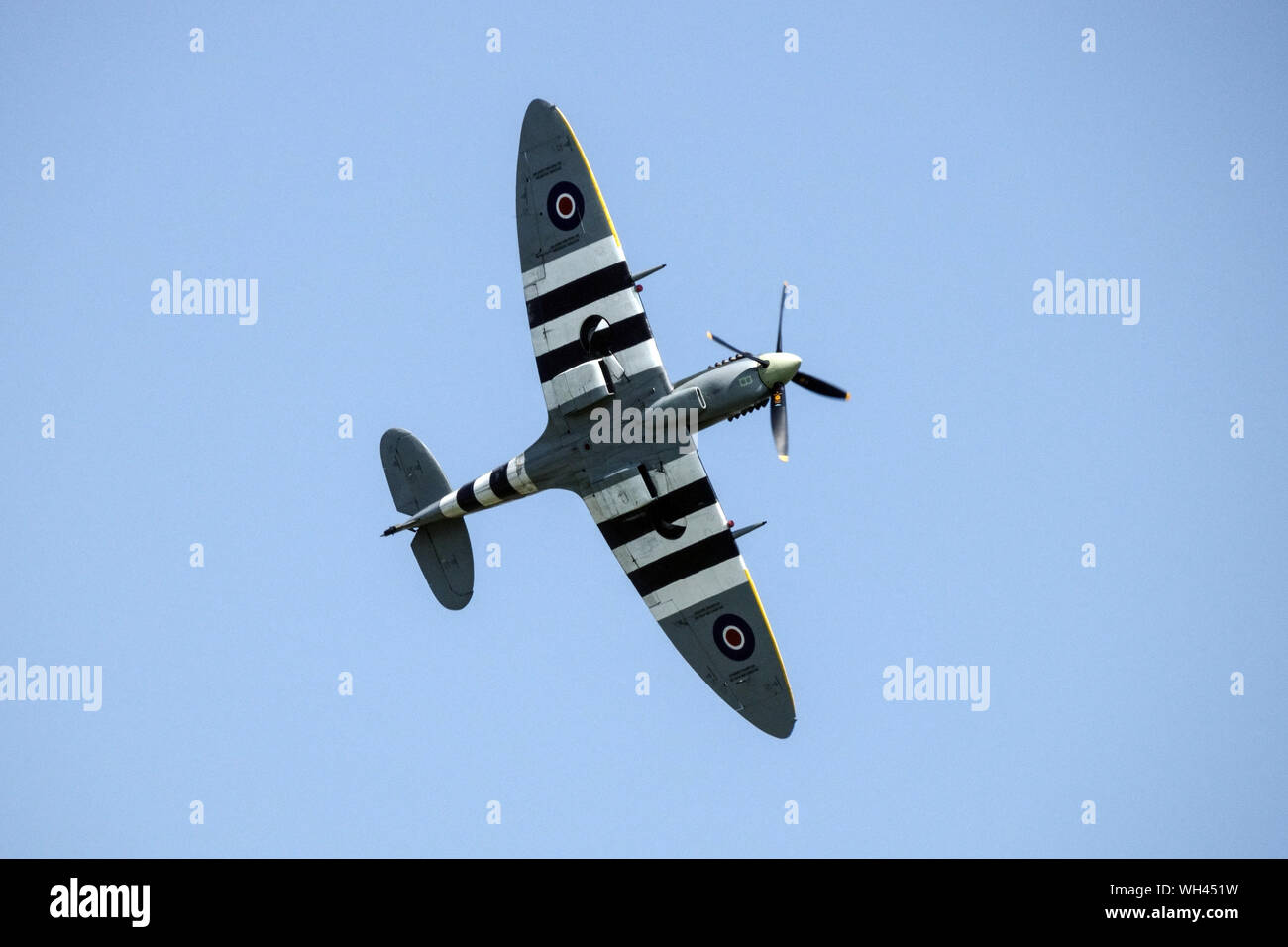 Supermarine Spitfire XV fighter flying, airplane on blue sky, view from below on striped wings Stock Photo