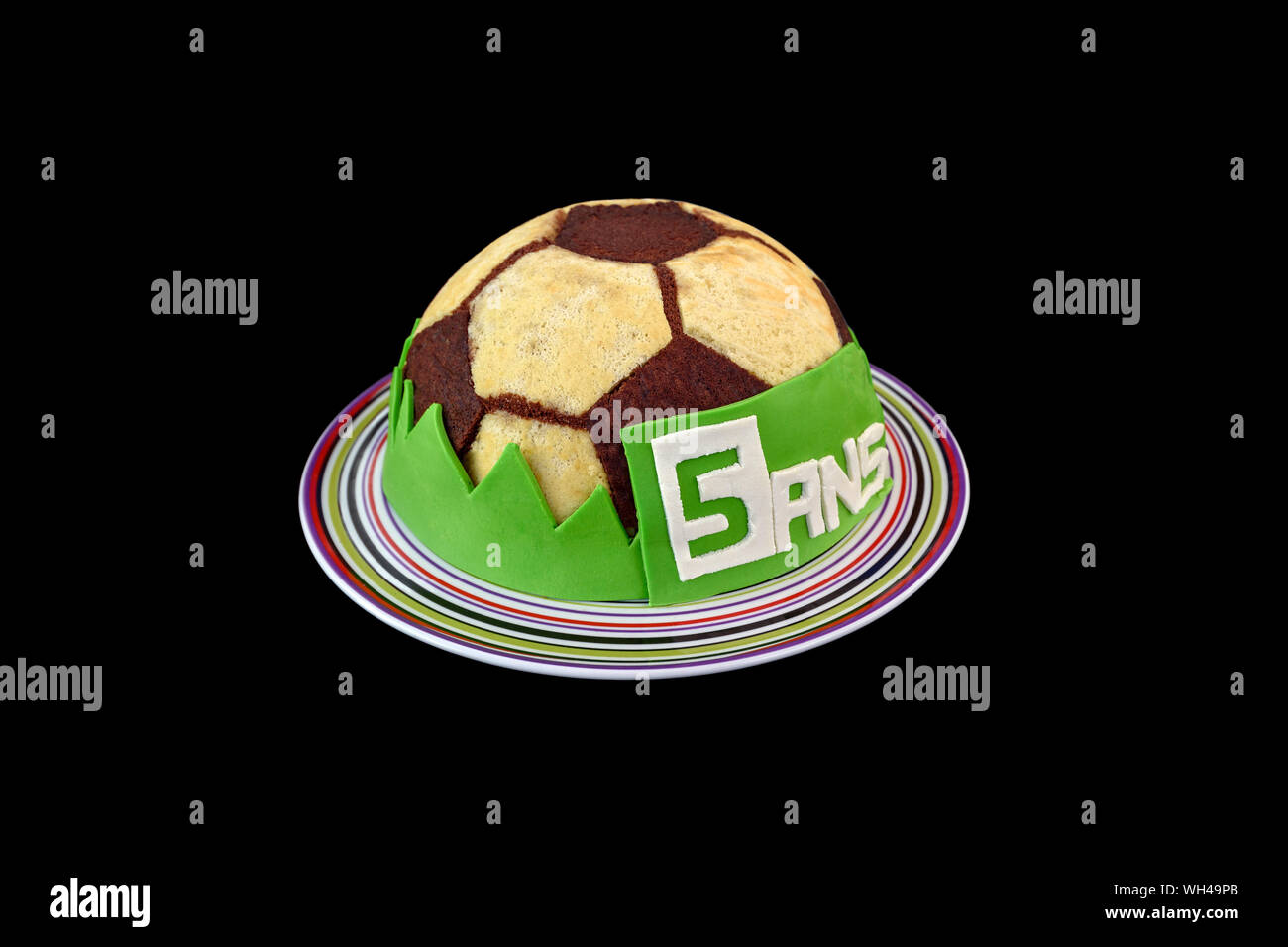 Beautiful soccer ball birthday cake for the fifth anniversary (5 years written in french '5 ans' on the cake), isolated on black background. Stock Photo