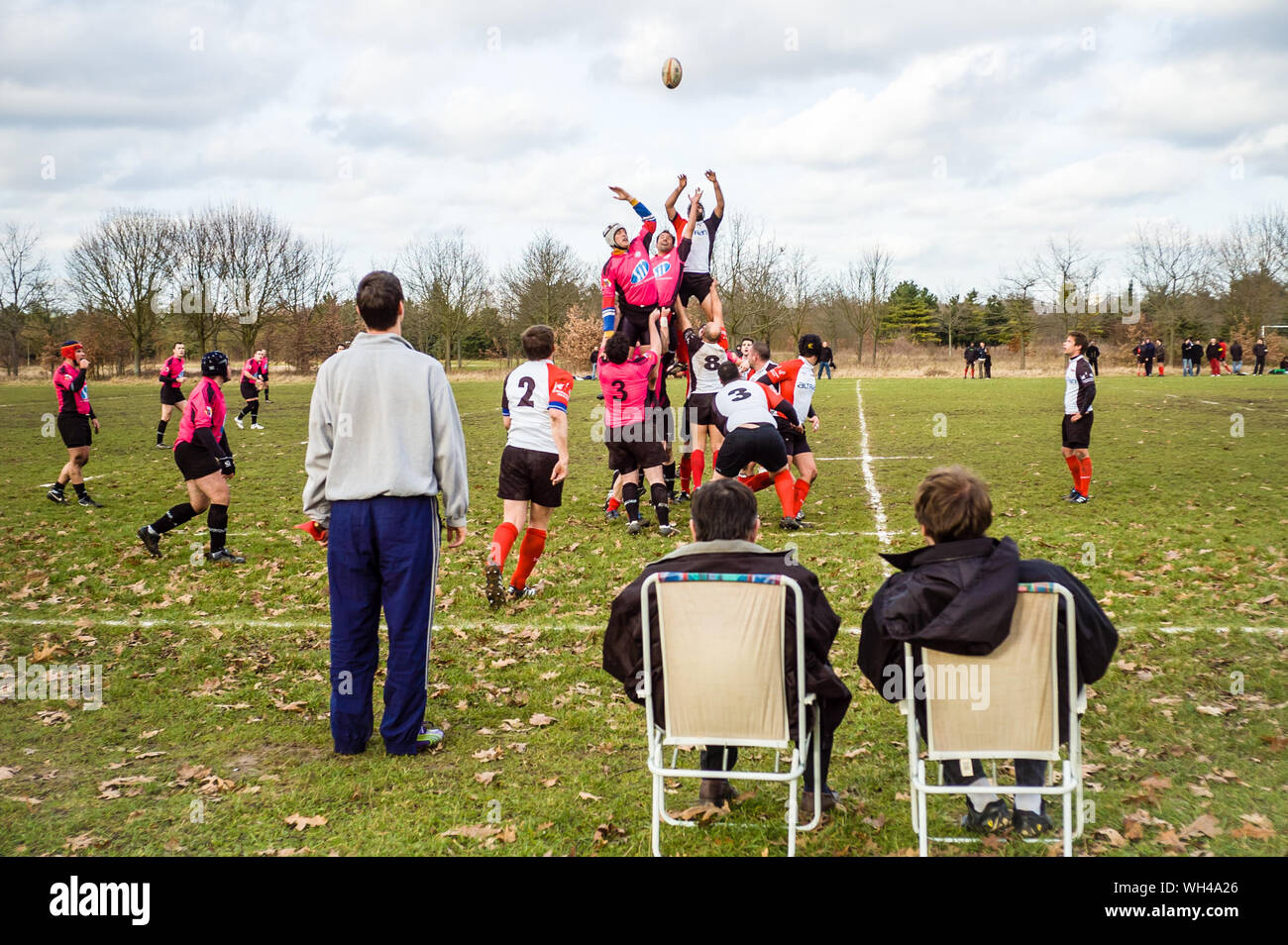 Spectators sitting on folding chairs watch a line-out during an amateur rugby match in the Bois de Vincennes in Paris by a cloudy winter sunday. Stock Photo