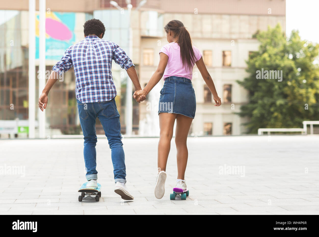 Happy african teenagers riding skateboards and holding hands Stock Photo