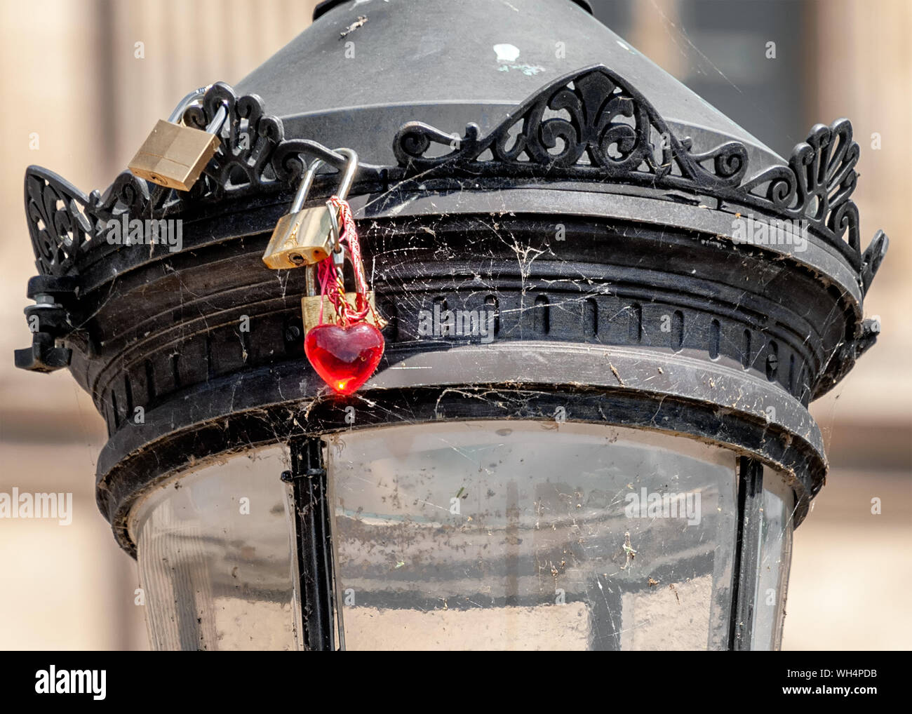 Old padlocks and a red heart key ring locked onto a lamppost covered with cobweb at ‘Pont des Arts’ pedestrian bridge in Paris. Stock Photo