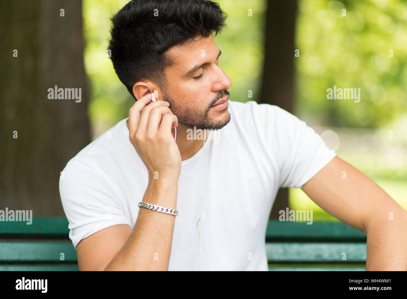 Man listening to music sitting ona bench in a park in a hot summer ...