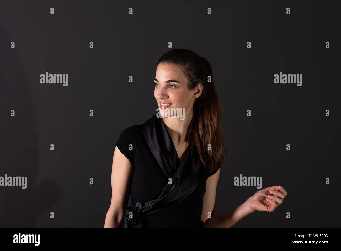A beautiful smiling young woman in an elegant black dress dancing in ...