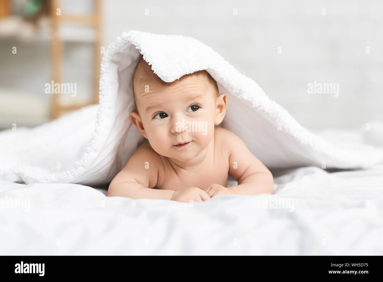 Adorable newborn baby crawling on bed and hiding under blanket Stock